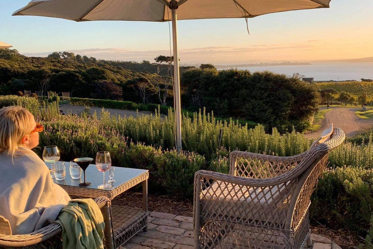 Girl sits at table during sunset and looks out on Waiheke Island